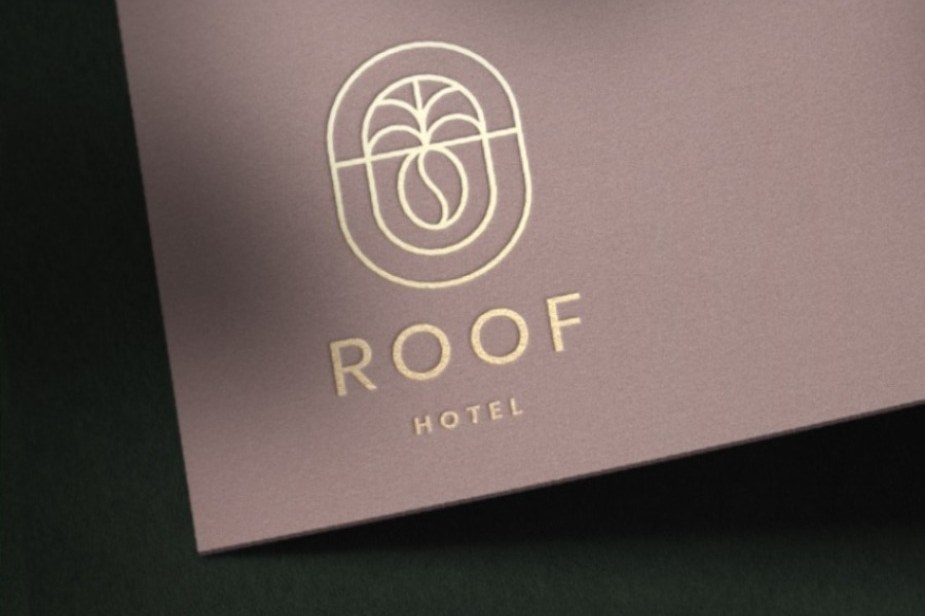 Foil-stamped ROOF Hotel logo and wordmark in gold on mauve paper, photographed under raking light